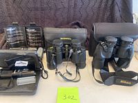 Lot items arranged side by side showing Nikon Aculon, Bushnell binoculars, and Shadowhawk flashlights with cases