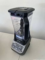 Side angle view of the full blender showing transparent pitcher with measurement markings and black handle and lid, sitting on metallic gray base.