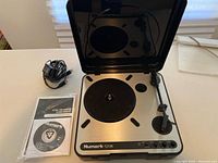 Portable Numark PT-01 USB turntable in open case with power cable, manual and software CD shown.