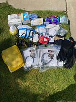 Full lot view showing an assortment of personal protective equipment including masks, gloves, hand sanitizer bottles, and packaged items laid on grass.
