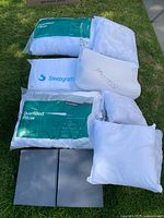 Photo showing six white pillows, some in packaging and one labeled bamboo memory foam pillow, arranged on grass and adjacent surface.
