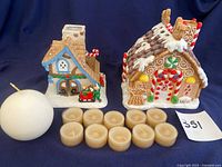 Front view of the Gingerbread and Santa Workshop ceramic tea light houses with 10 small white tea lights and a white round candle arranged in front