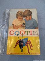 Front of vintage Cootie game box showing children playing with the toy bug and colorful title.