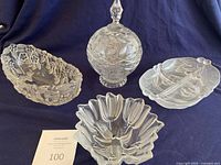 Four vintage frosted and etched crystal and glass serving dishes including candy dish with lid, oval bowl, tulip candy bowl, and relish tray, displayed on cloth background.