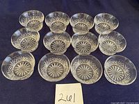 Twelve clear cut glass finger bowls arranged on a dark cloth showing starburst pattern at base