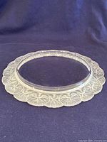 Front view of the round glass dish featuring clear center and frosted floral embossed rim on dark background