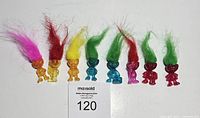 Eight alien troll doll pencil toppers arranged in a row, showing various colors of translucent bodies and hair colors including pink, red, yellow, and green.