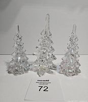 Front view of three clear art glass Christmas trees on a white background, showing two candle holders and one decor tree.