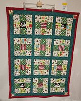 Full view of the Christmas themed baby quilt with patchwork squares and red green border.