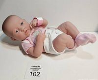 Full body image of Berenguer baby doll in pink onesie and white diaper lying on side.