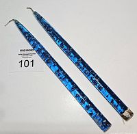 Two blue lucite tapered candles laying flat showing embedded metallic flecks and wick ends.