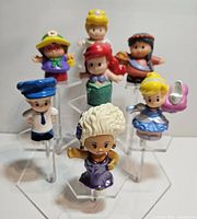 Front view of seven modern Fisher Price Little People figures displayed on hexagonal clear plastic stands.