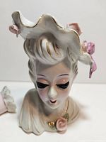 Close-up view of the lady head vase showing the facial features, white hat with pink roses, and gold accents.