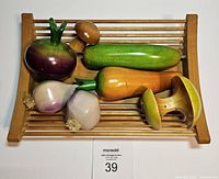 Top view of all wooden fruit figurines arranged on teak wood slatted tray, showing carrot, cucumber, beet, turnips, and mushrooms.