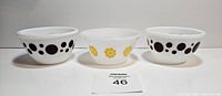 Three milk glass bowls shown side by side with different patterns: two with black circles, one with yellow flowers.