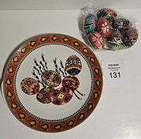 Lot showing West German painted egg plate with intricate orange and black border and central painted egg design, alongside bagged Ukrainian hand-painted eggs.