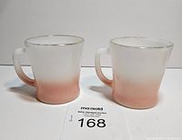 Two vintage Fire King mugs made of pink and white gradient milk glass with silver rims, shown side by side.