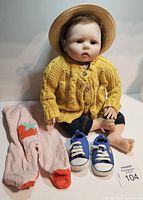 Front view of reborn doll wearing yellow cardigan, denim pants, blue shoes, and pink pajama pants next to it
