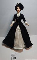 Barbie doll wearing midnight blue velvet coat and cream satin dress with black hat, in standing pose