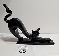 Glossy black stylized resin cat statue stretching on base.