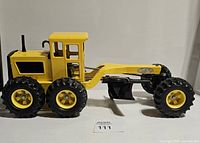 Side profile of the vintage Tonka metal road scraper showing the yellow cab, six large black tires, and articulated blade.