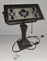 Front view of the Toronto Maple Leafs stained glass desk lamp showing rectangular shade with logo and metal base with pull chain switch.
