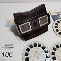 Photo of vintage black Bakelite View-Master viewer with three View-Master reels visible around it, reels include Calgary Stampede and Queen Elizabeth II coronation reels.