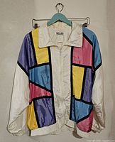 Front view of vintage parachute jacket with block colors pink, purple, yellow, turquoise, and white with black lines, on a hanger.