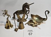 Lot of vintage brass decor items including unicorn, dinosaur with stunted tail, swan bowl, bull, and two bells shown together.