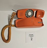 Top view of vintage orange rotary dial telephone with coiled cord and rotary dial.