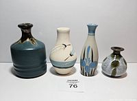 Four vintage small pottery vases of different shapes and colors displayed side by side, showing size and color variations.