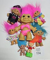 Full view of 8 vintage Troll dolls in various hair colors, sizes, and outfits laid out on white surface.