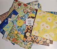 Top view of a pile of vintage floral themed wrapping paper sheets showing varied colors and patterns including yellow daisies, multi-color florals, and geometric designs.