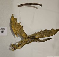 Handcrafted wooden dragon mobile suspended by strings from a natural wooden branch. Dragon painted yellowish-brown with detailed wings and scales.