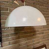 Side view of white semi-sphere pendant lamp hanging against brick wall