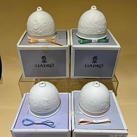 Front view of four Lladro bells on boxes showing ribbons and relief designs