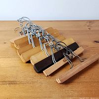 Nine wooden clamp hangers in staggered stack showing metal hardware and felt pads