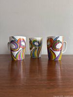 Front view of three vintage ceramic mugs with colorful swirl designs lined up from left to right.