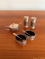 Full set on wooden table showing two shakers, mustard pot with lid closed, two oval dishes and three spoons
