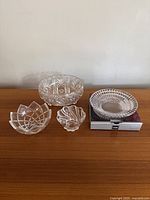 Four crystal and glass bowls displayed on wooden surface against white wall, showing entire set