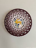 Full view of ceramic wall plate showing maroon pierced lace-like border and central yellow deer with blue flowers on white background.