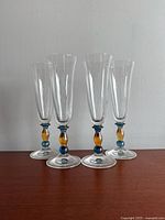 Four vintage champagne flutes standing upright, showing front view on a white surface and neutral background. Flute stems have blue and amber glass spheres.