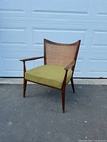 Side angle view of wooden mid-century armchair showing cane back and green cushioned seat with wear on wood.