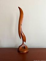 Front view of the teak bird figurine showing its height and curved beak, standing on a round base.