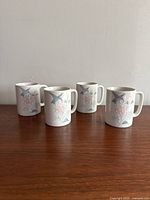 Front angle showing all four Otagiri mugs with hummingbird and flower design spaced apart on wood surface.