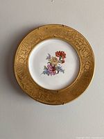 Front view of the decorative plate showing floral center and gold ornate border