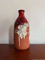 Front view of the signed vintage ceramic vase showing the red upper glaze, brown base, and textured white floral design.
