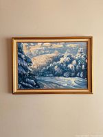 Full view of the framed oil painting depicting a snowy winter landscape with trees and a distant church, hung on wall.