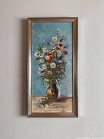 Full view of vertical floral painting in narrow wood-toned frame hung on wall.