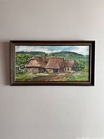 Full view of the framed vintage oil painting showing countryside scene with cottages, trees, and grassy landscape.